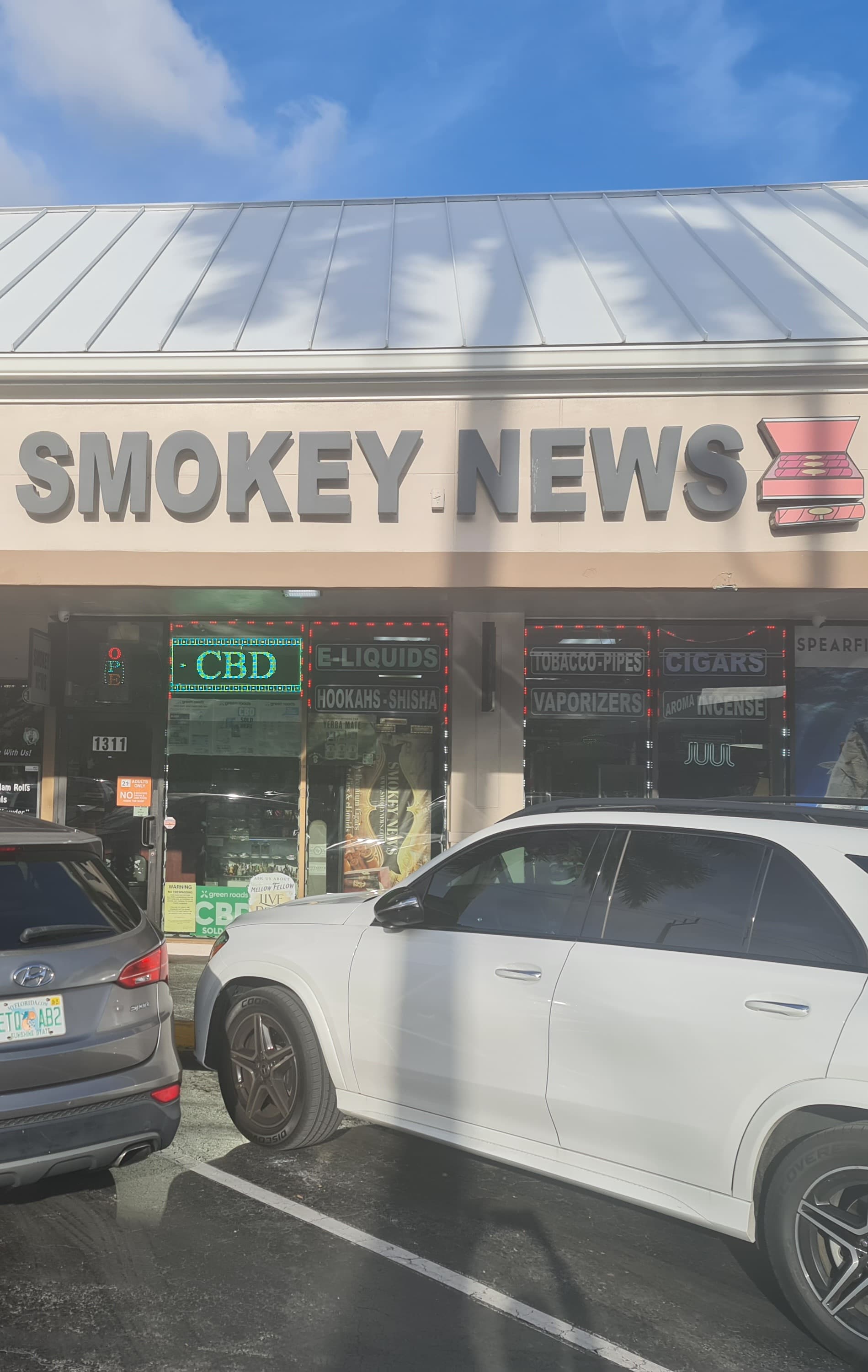 Smokey News storefront at 1311 SE 17th Street in Fort Lauderdale — the brushed-metal sign and window of cigars, hookahs, and vapes